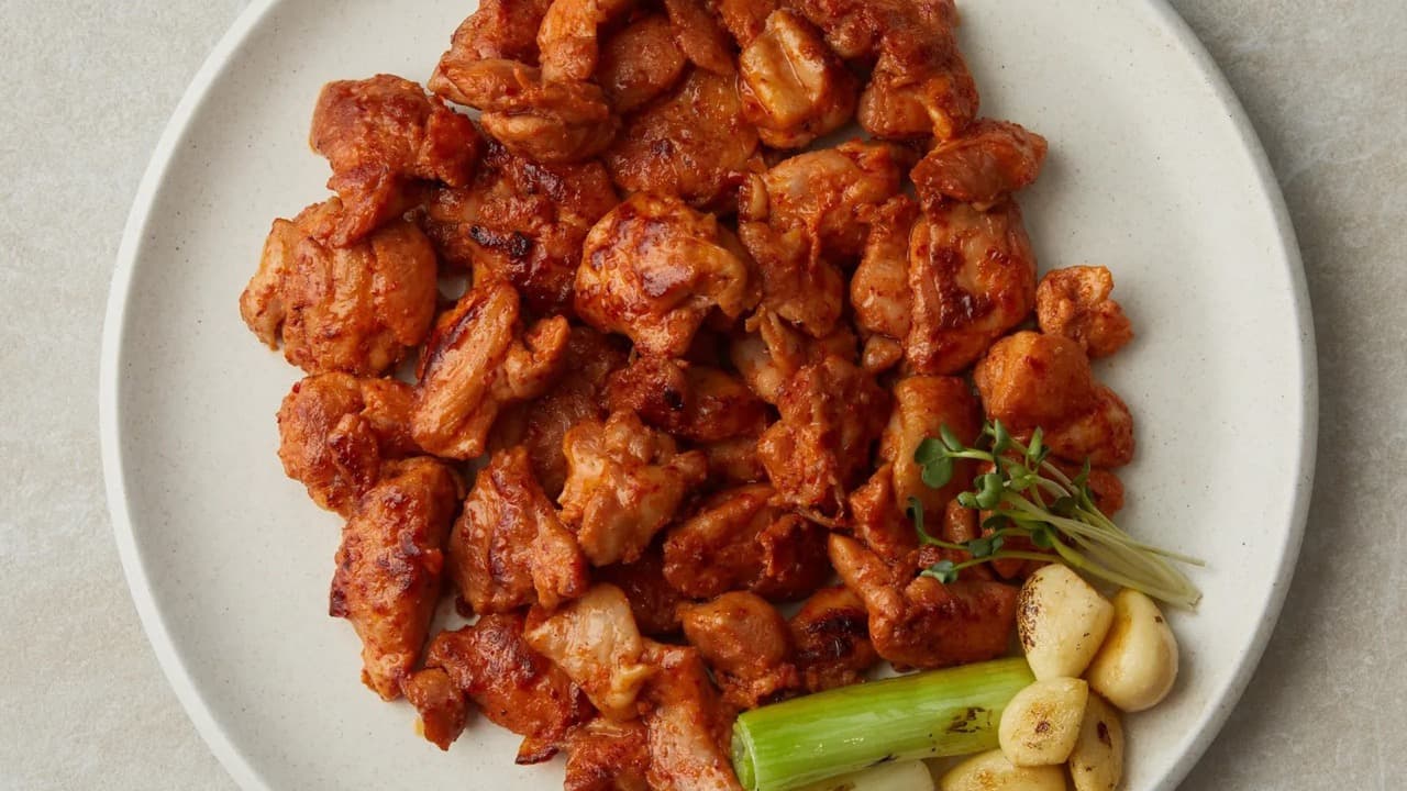 흰 접시에 담긴 매콤한 닭갈비와 구운 마늘·대파
